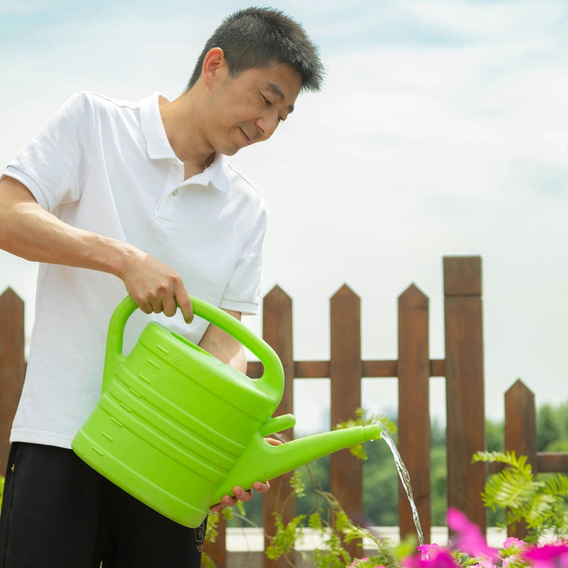 Man watering plants with a green watering can outdoors.