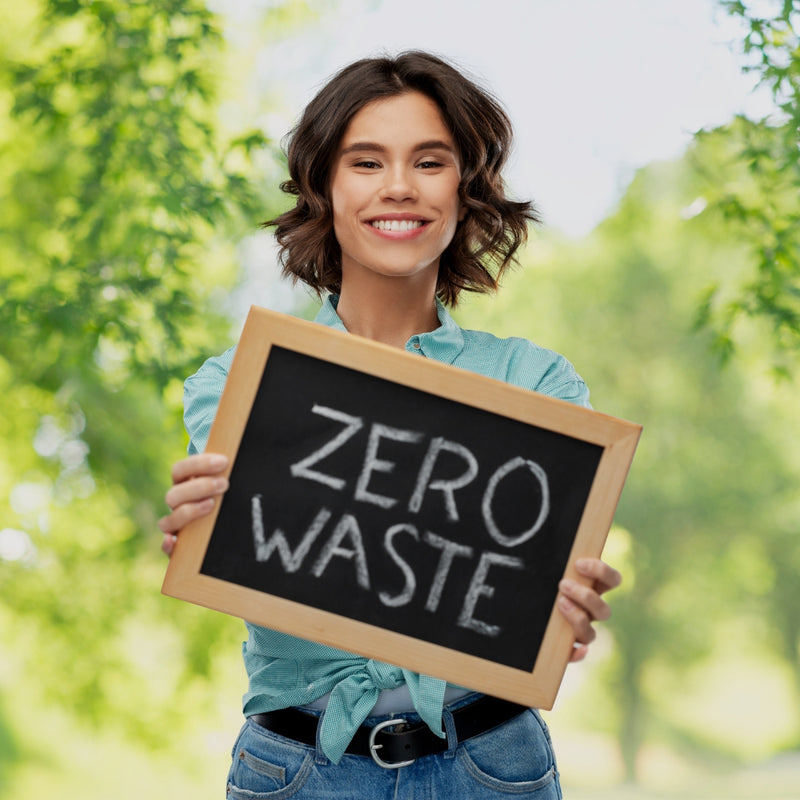 Woman holding a sign that says 'Zero Waste' with a green, outdoor background